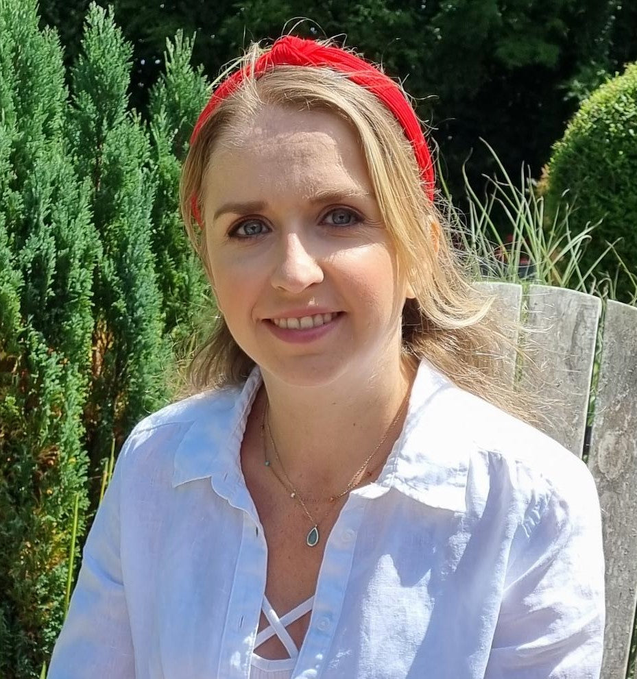 Woman nutritionist wearing a red headband and white shirt outdoors with greenery in the background