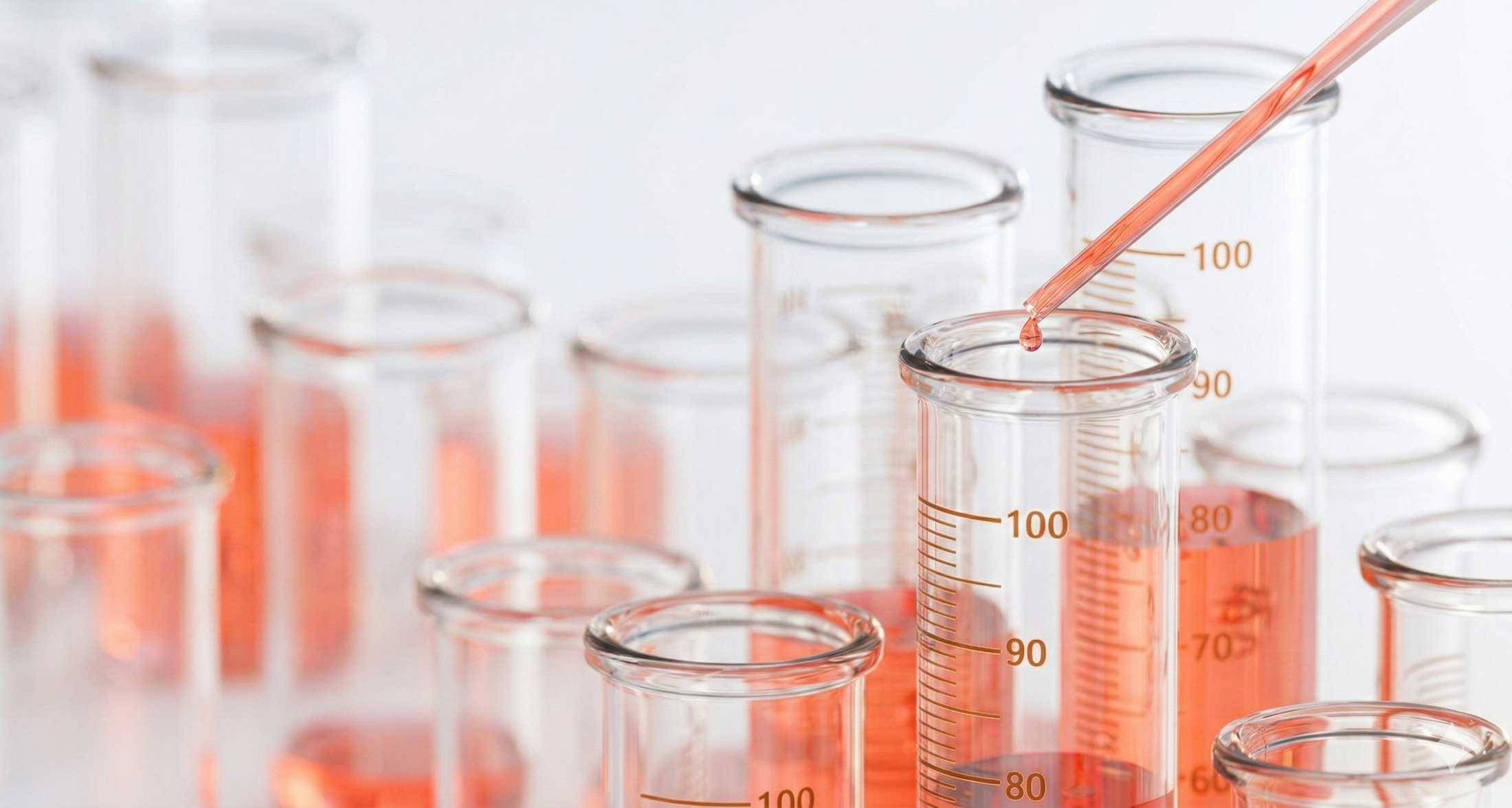 Laboratory beakers with red liquid and a pipette on a light background